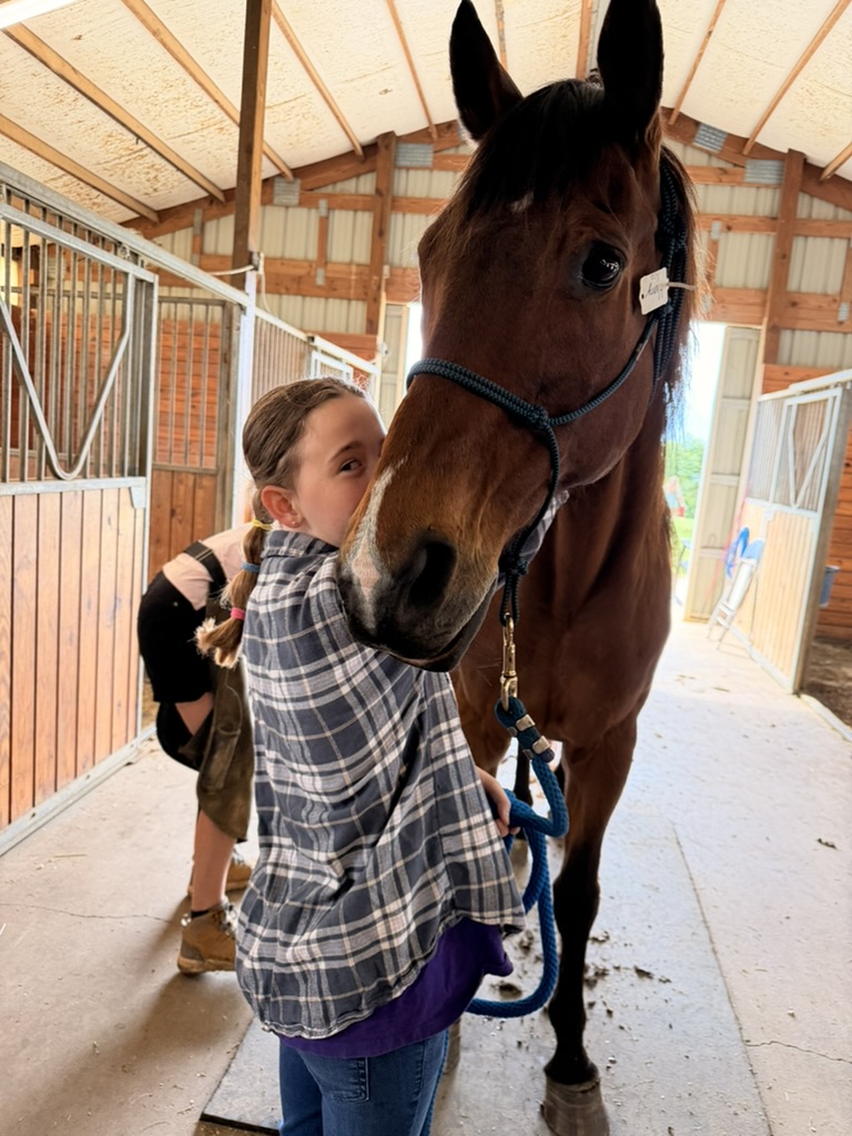 Evie with her cheek against Henry's face in the barn aisle