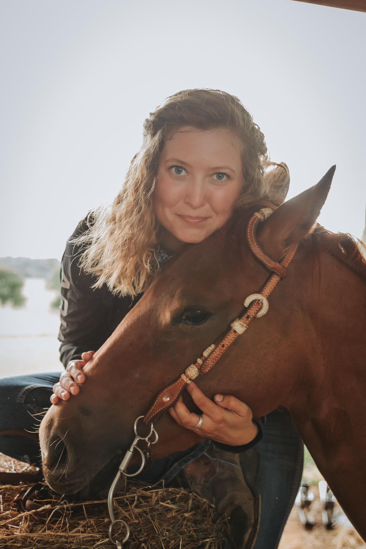 Meg crouched cheek-to-cheek with one of the horses resting in the barn