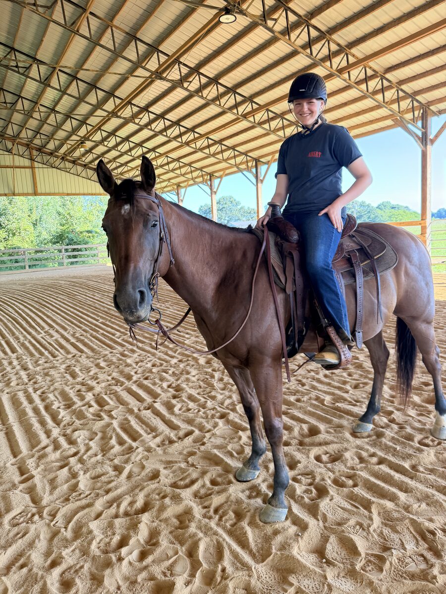 A camper riding a bay horse in the covered arena at Gracewood Acres