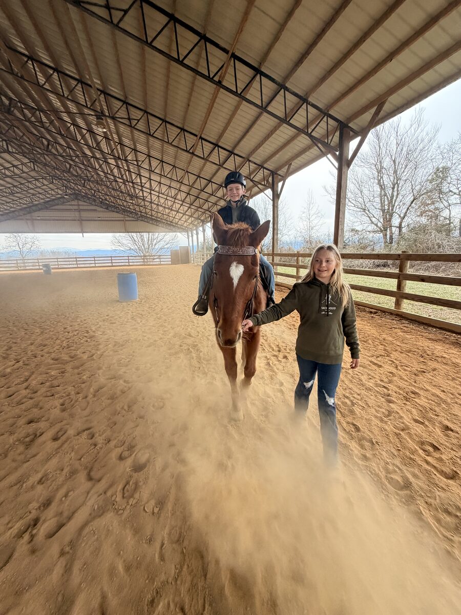 A young helper leading a rider on horseback through the covered arena