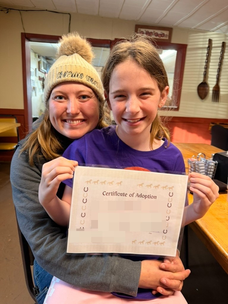 Evie holding her Certificate of Adoption for Mr. Henry Boy, with Meg in a Gracewood Stables beanie